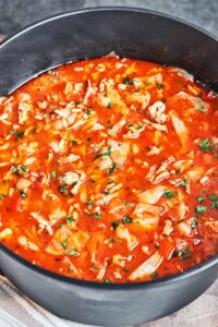 Cabbage roll soup with ground beef and rice in a deep pot, filled with tender cabbage and carrots in tomato broth and sprinkled with fresh parsley.
