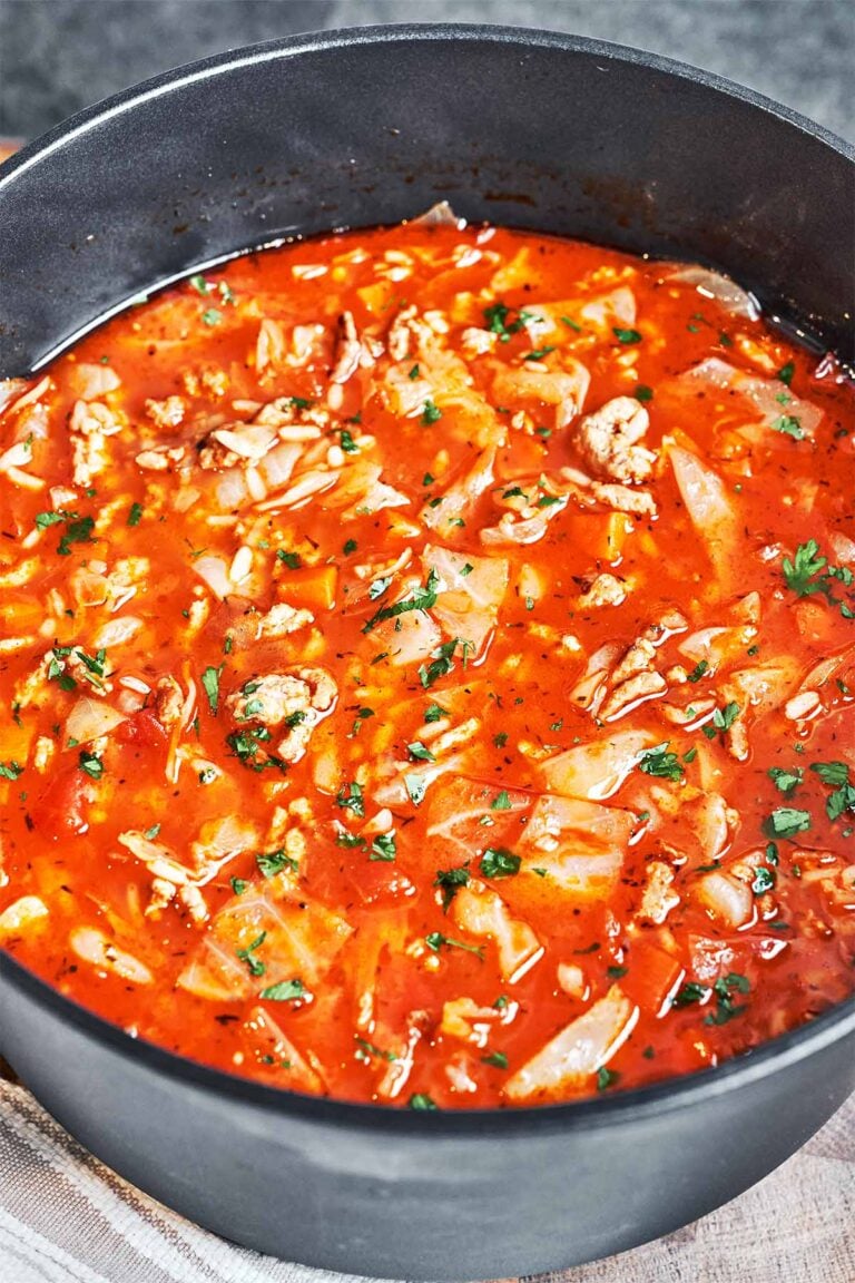 Cabbage roll soup with ground beef and rice in a deep pot, filled with tender cabbage and carrots in tomato broth and sprinkled with fresh parsley.