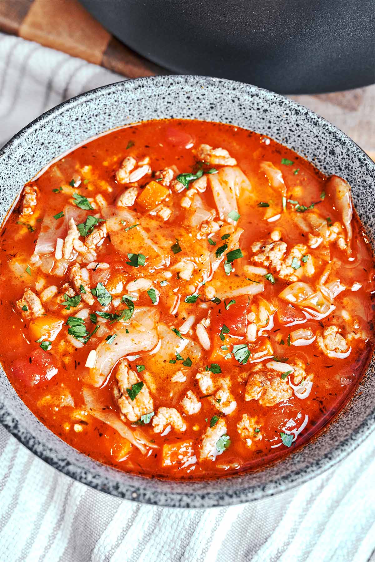 Cabbage roll soup with ground beef, rice, and tender cabbage in a rich tomato broth, finished with fresh parsley in a speckled bowl.
