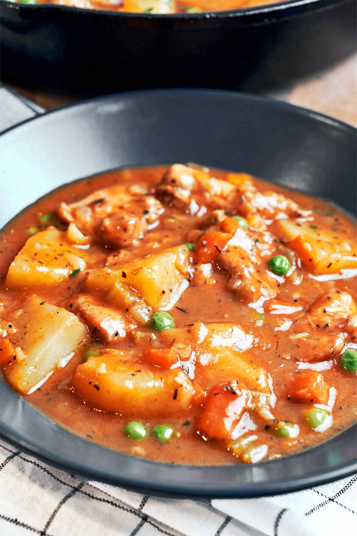 A cozy bowl of chicken stew with tender potato chunks, carrots, peas, and juicy chicken in a rich, glossy savory sauce.