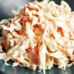 Creamy coleslaw with thin ribbons of cabbage and carrot tucked into a silky mayonnaise and sour cream dressing, served on a dark plate.