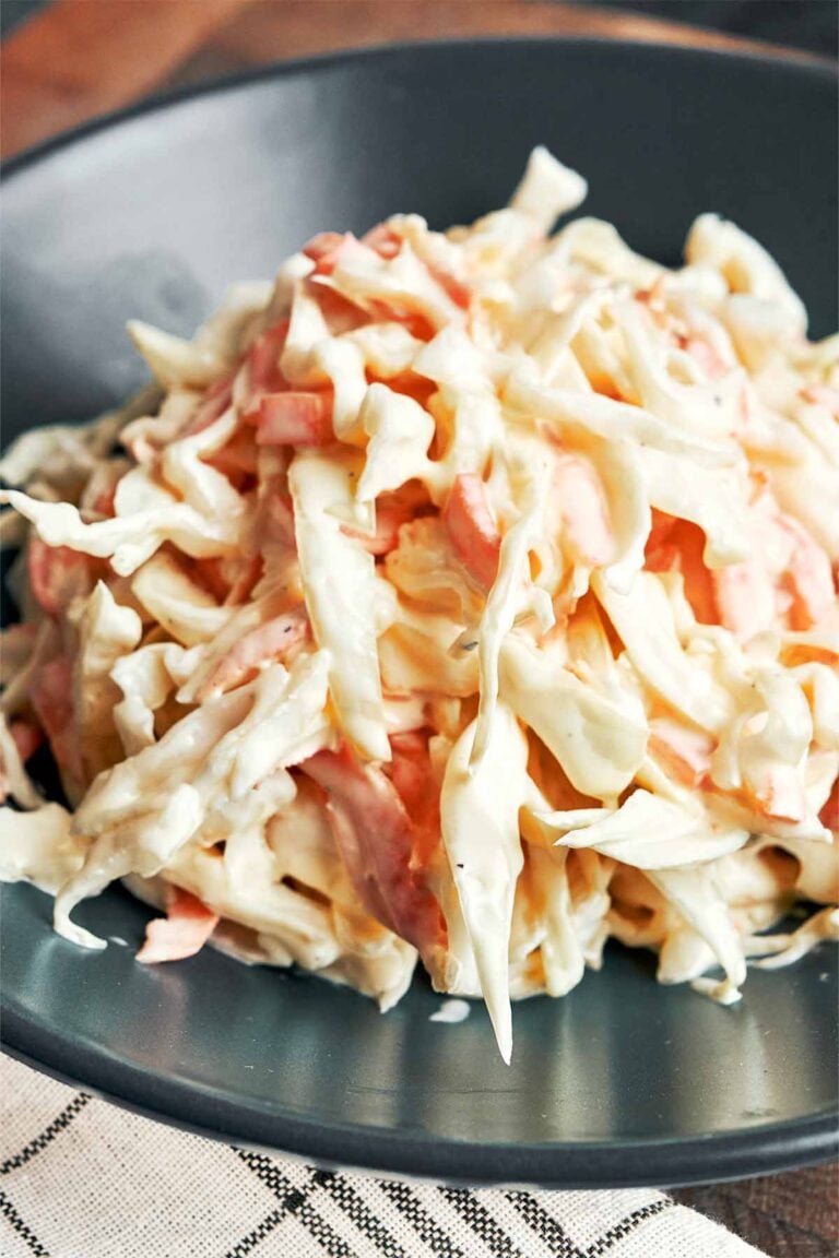 Creamy coleslaw with thin ribbons of cabbage and carrot tucked into a silky mayonnaise and sour cream dressing, served on a dark plate.