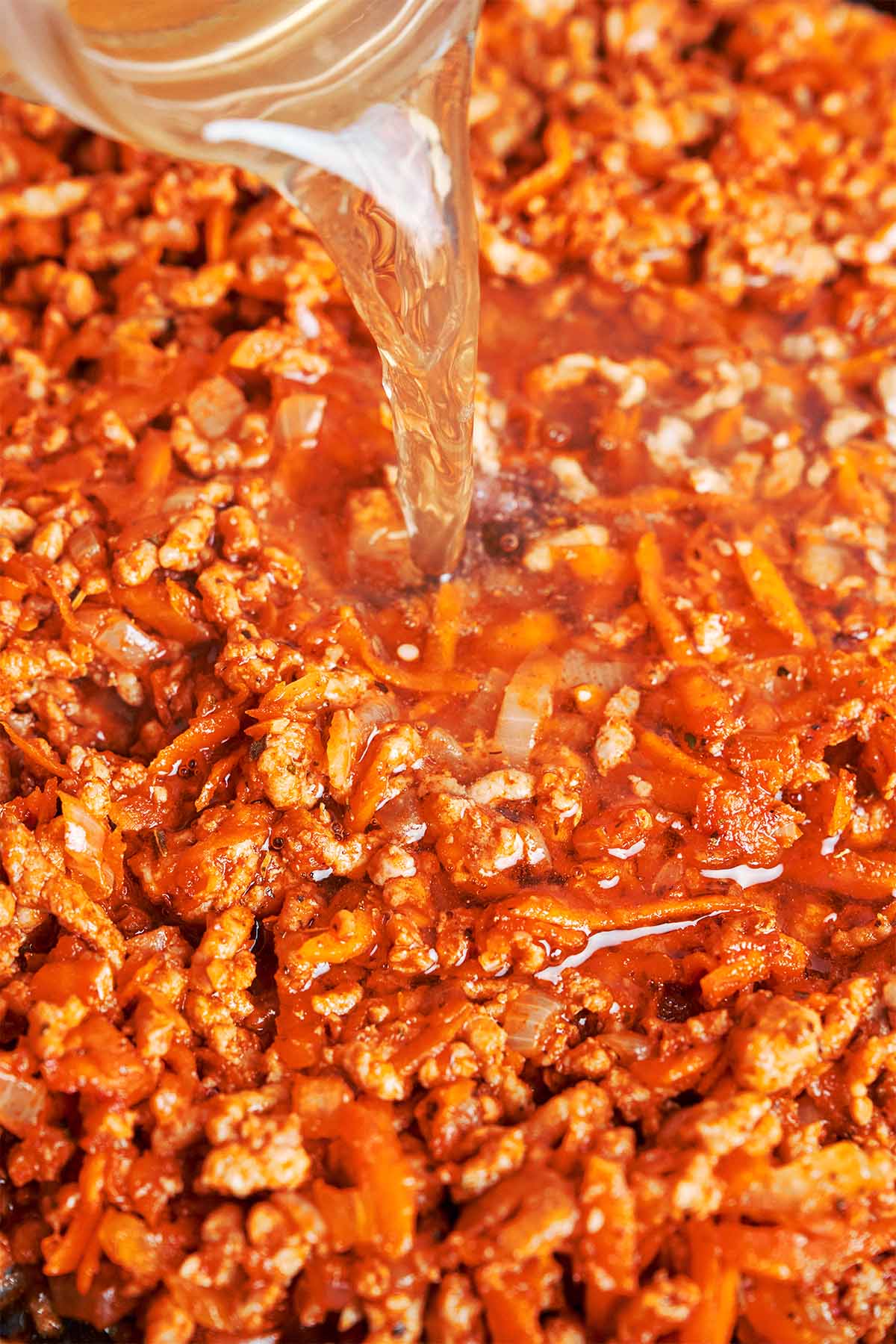 Beef broth poured into the seasoned beef and vegetable mixture, loosening the rich tomato base before the cabbage goes in.