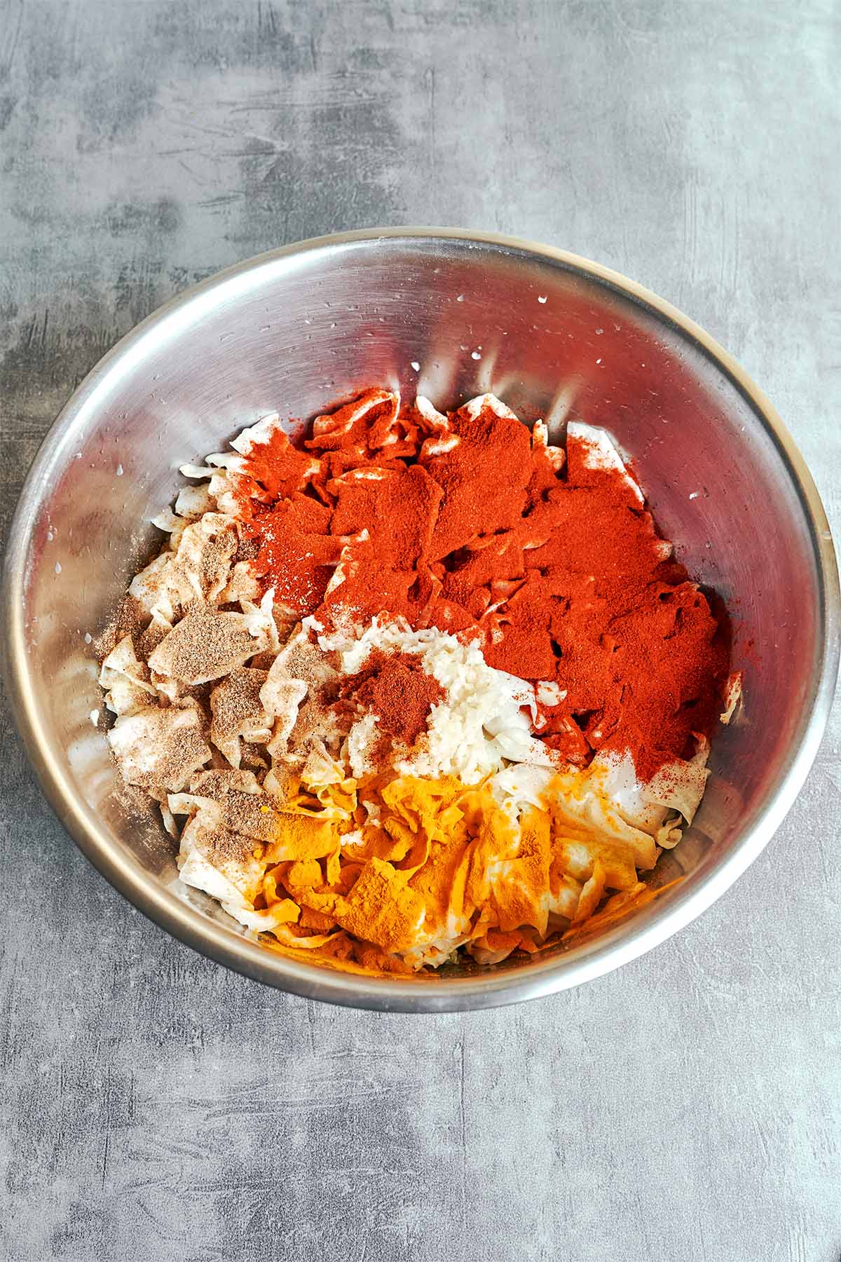 Cabbage topped with sweet paprika, golden turmeric, ground coriander, and a mound of minced garlic and chili, ready for the hot oil.