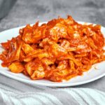 Spicy marinated cabbage salad with glossy paprika and garlic dressing, heaped on a white plate beside a striped linen napkin.