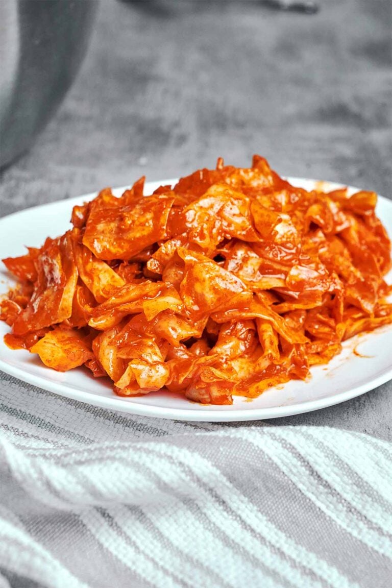 Spicy marinated cabbage salad with glossy paprika and garlic dressing, heaped on a white plate beside a striped linen napkin.