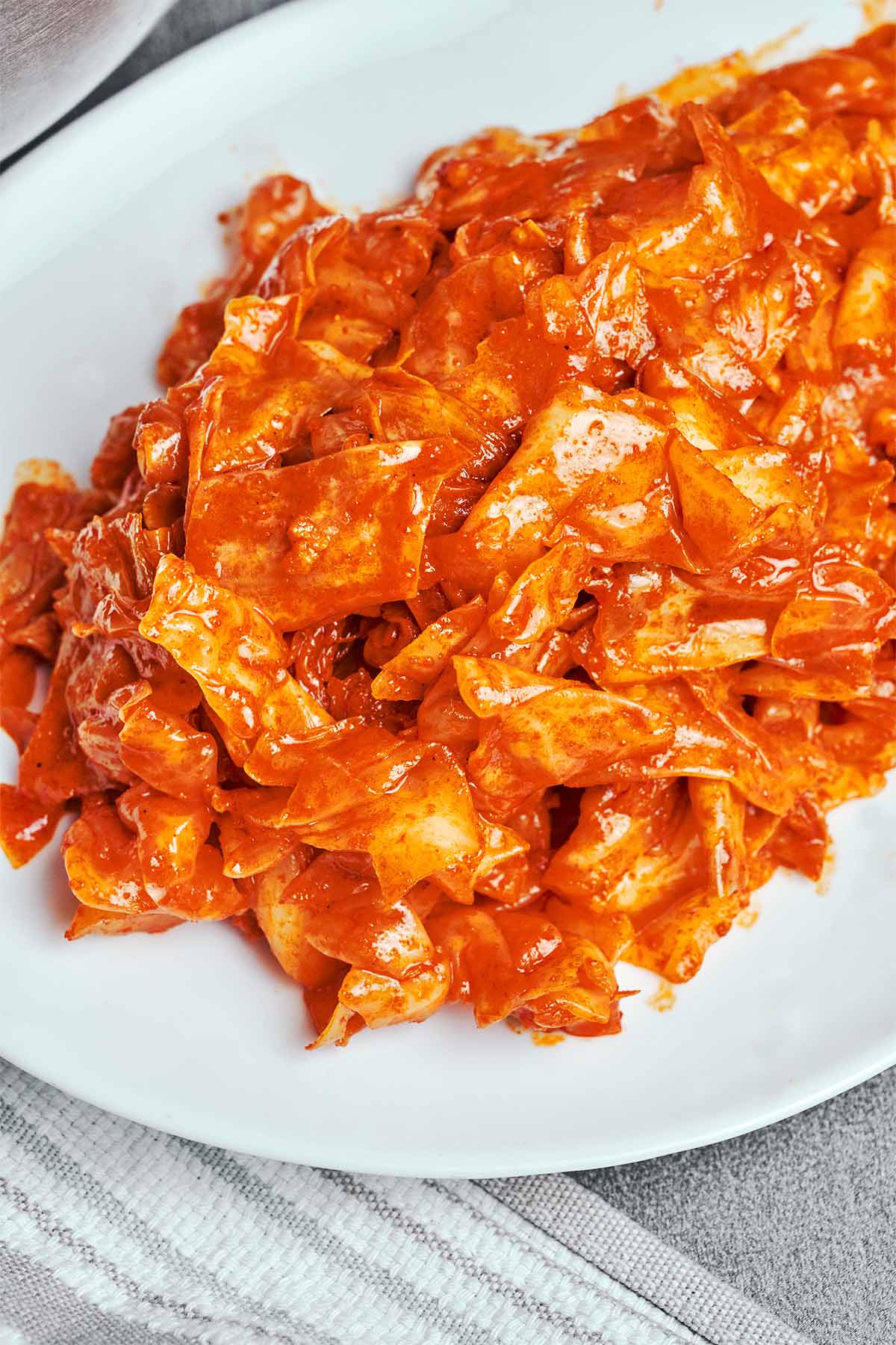 Spicy marinated cabbage salad piled onto a white plate, with glossy red dressing clinging to the crinkled leaves.