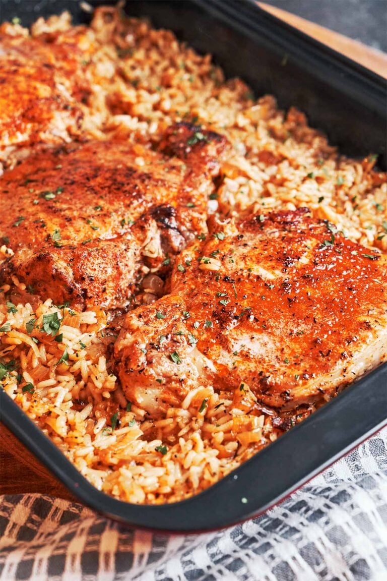 Baked Pork Chops and Rice with juicy golden pork chops over savory, fluffy rice finished with fresh parsley.