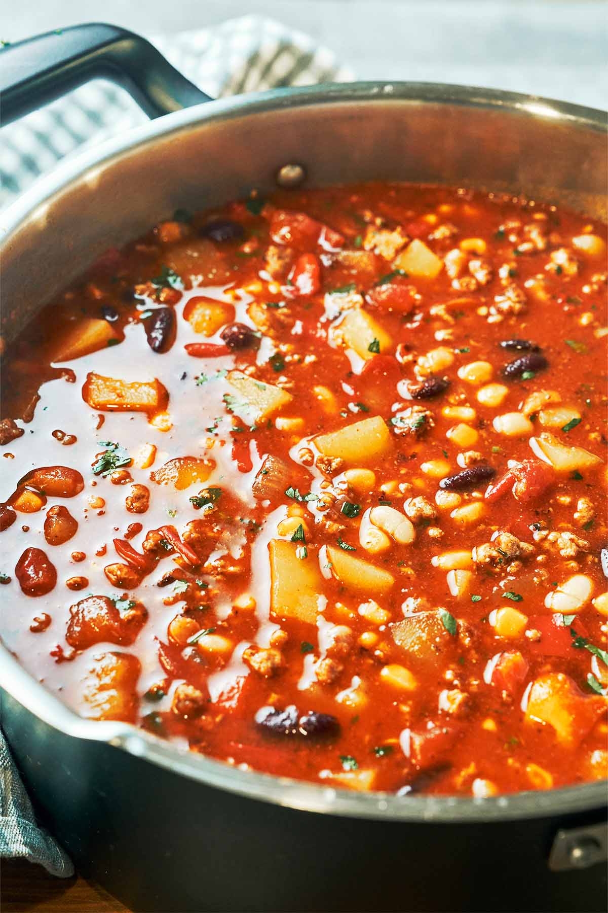 A pot of hearty, homemade soup filled with tender potatoes, ground beef, beans, and sweet corn in a rich tomato broth, finished with fresh herbs.