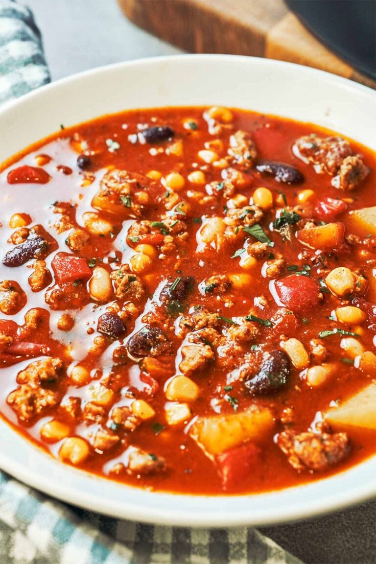 A cozy bowl of homemade Cowboy Soup, loaded with savory ground beef, tender potatoes, pinto and kidney beans, sweet corn, and red bell pepper in a rich, smoky tomato broth, finished with fresh parsley.