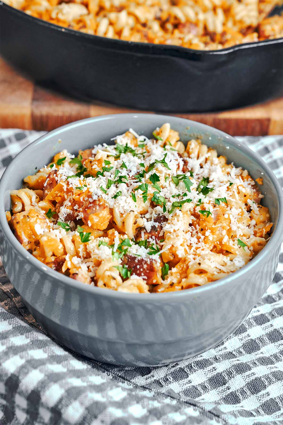 A gray bowl filled with fusilli in creamy pumpkin sauce and golden bacon, finished with grated Parmesan and chopped parsley.