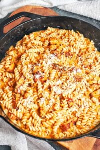 Creamy pumpkin pasta with bacon, tender fusilli, and a sprinkle of Parmesan, ready to serve from a cast iron skillet.