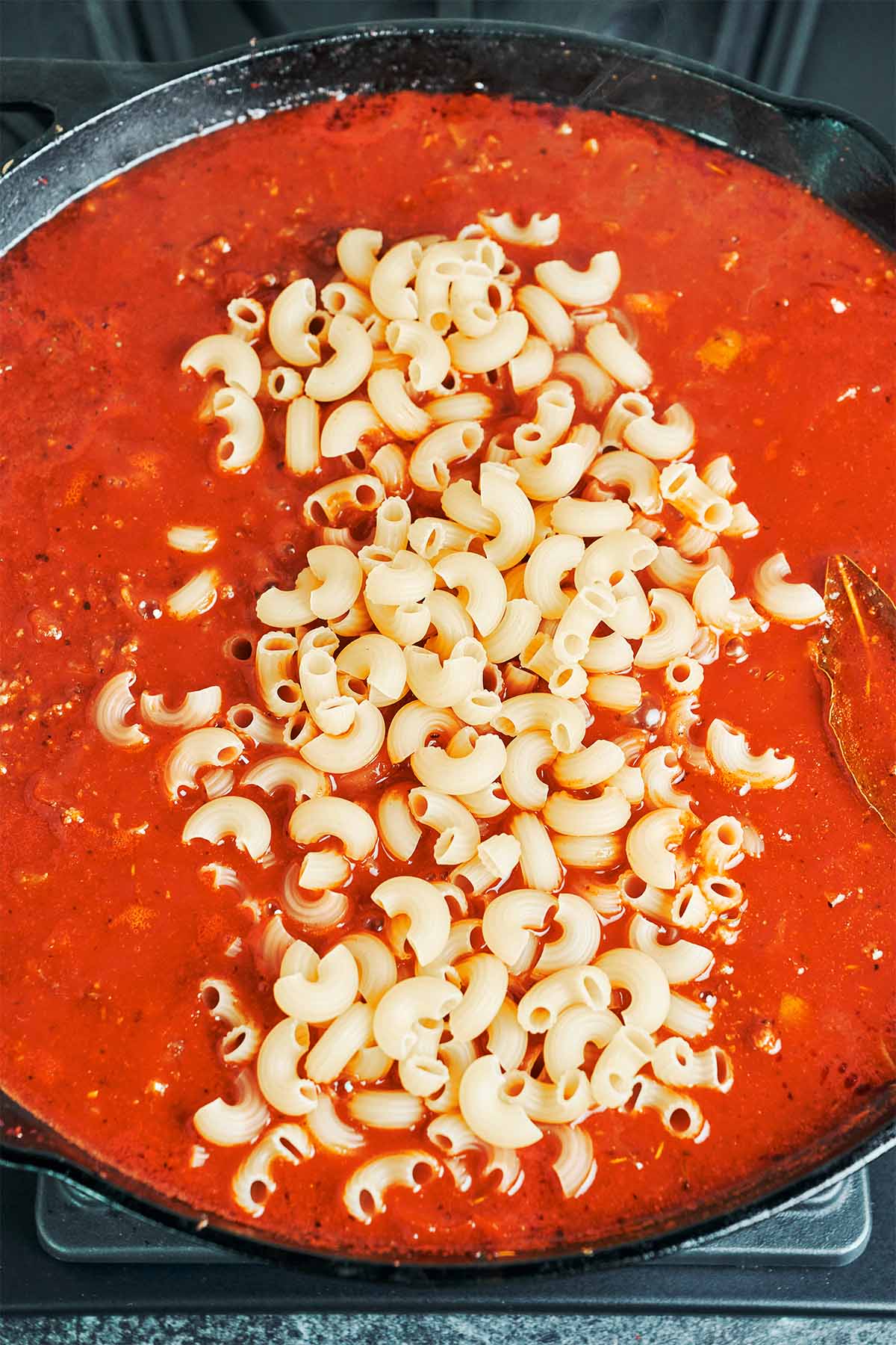 Uncooked elbow macaroni scattered into the simmering tomato and beef sauce, ready to cook right in the skillet.