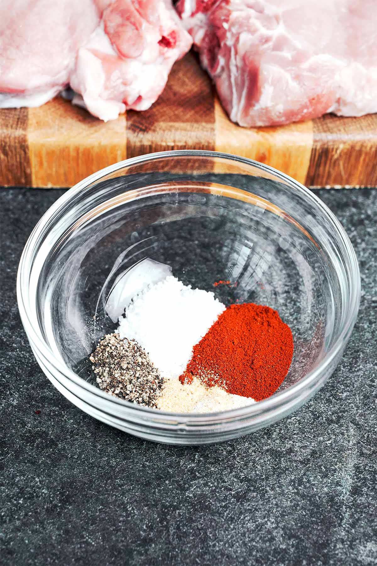Paprika, garlic powder, onion powder, salt, and black pepper measured into a glass bowl, ready to season the bone-in pork chops.