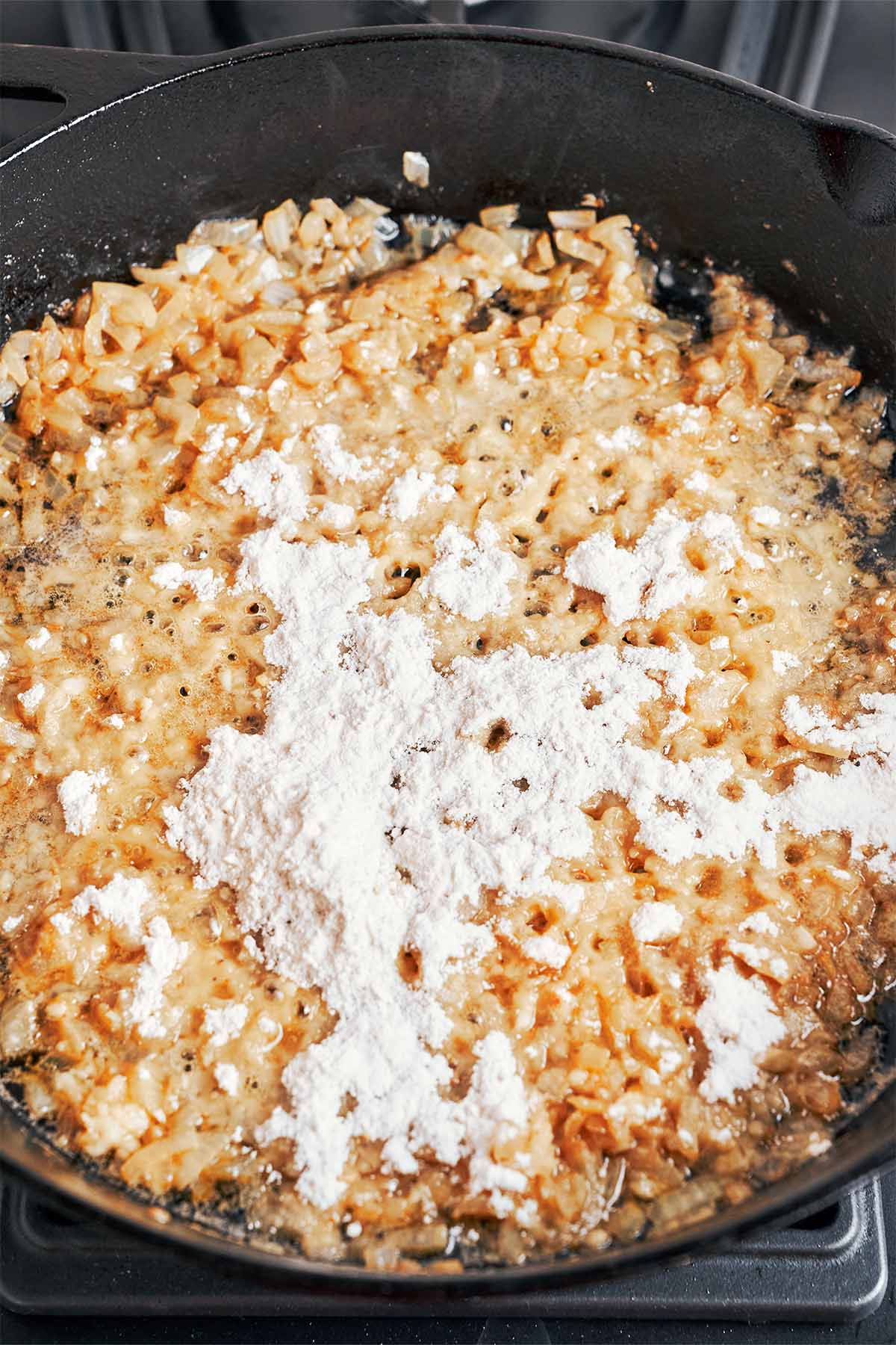 Flour sprinkled over the softened onions and garlic in the skillet, ready to thicken into a rich homemade gravy.