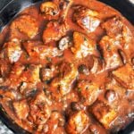 Pork stew with mushrooms in a cast-iron skillet, with tender pork shoulder, rich gravy, and a scattering of fresh parsley.