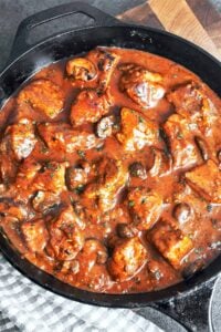 Pork stew with mushrooms in a cast-iron skillet, with tender pork shoulder, rich gravy, and a scattering of fresh parsley.