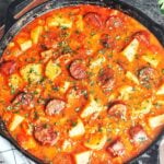 Sausage and potato stew in a cast iron skillet, with golden-brown smoked sausage, tender potato chunks, and fresh parsley in a rich paprika sauce.