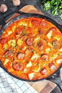 Sausage and potato stew in a cast iron skillet, with golden-brown smoked sausage, tender potato chunks, and fresh parsley in a rich paprika sauce.