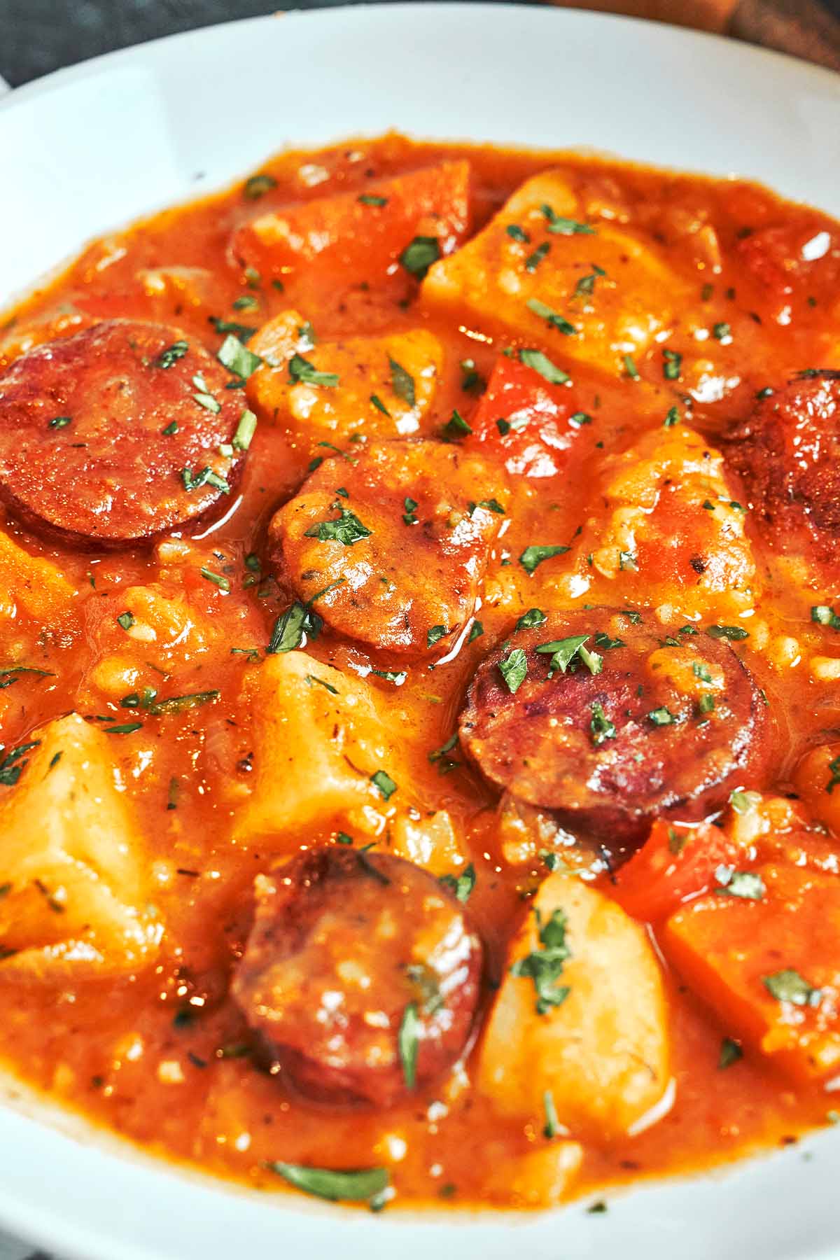 A bowl of tender potatoes and browned smoked sausage coated in thick paprika sauce, finished with a scattering of fresh parsley.