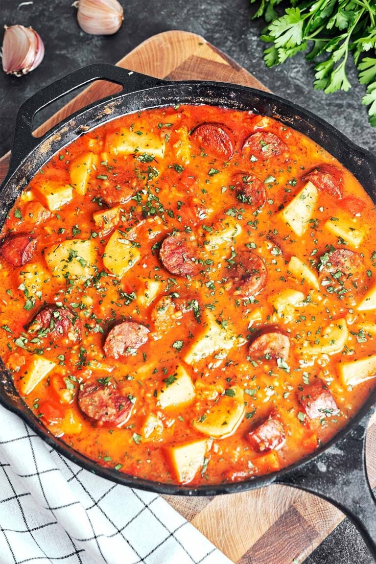 Sausage and potato stew in a cast iron skillet, with golden-brown smoked sausage, tender potato chunks, and fresh parsley in a rich paprika sauce.