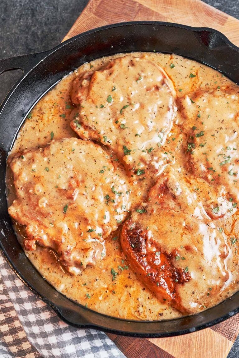 Smothered pork chops in rich onion gravy, finished with fresh parsley in a cast-iron skillet.