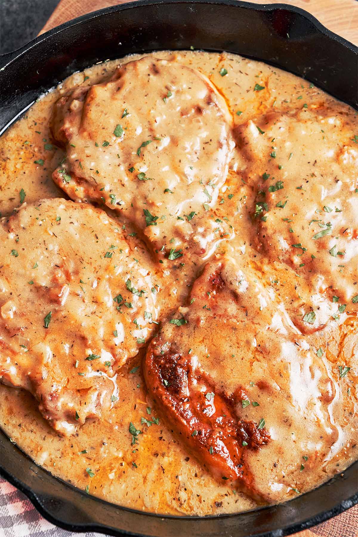 Tender smothered pork chops covered in rich onion gravy and finished with fresh parsley in a cast-iron skillet.