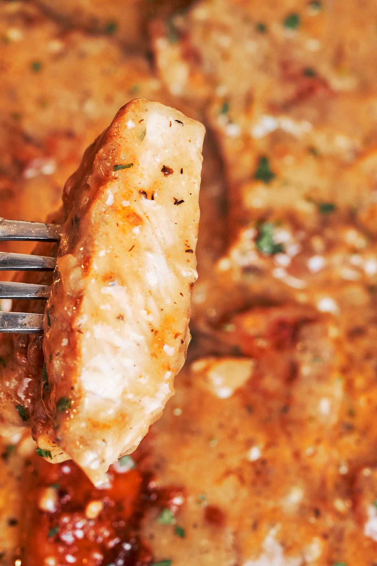 A juicy slice of pork chop lifted on a fork, showing the tender center with rich onion gravy in the background.